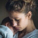 Mlada majka drži bebu u naručju i izgleda zabrinuto