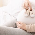 Trudnica drži bebine patikice na stomaku tokom pripreme za dolazak bebe