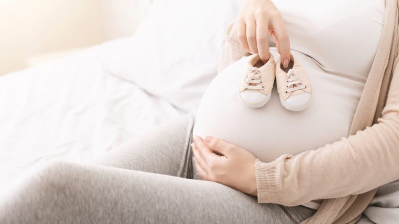 Trudnica drži bebine patikice na stomaku tokom pripreme za dolazak bebe
